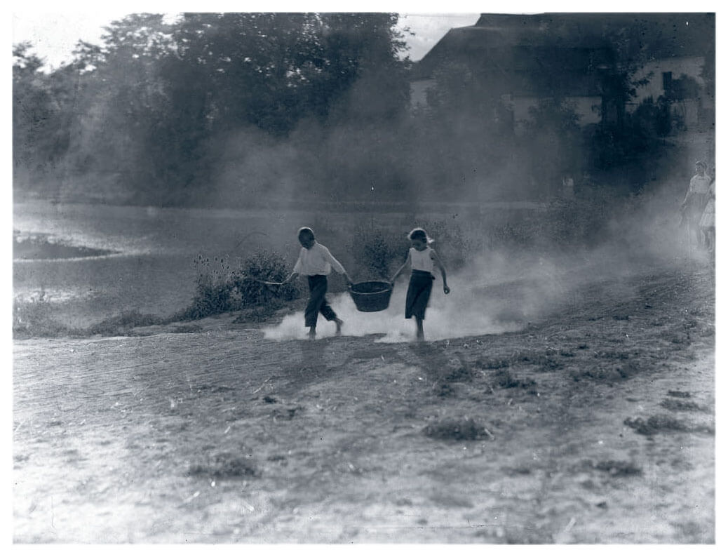 Two farm children running in bare feet holding a basket between them