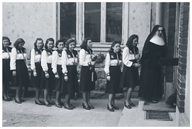 A line of Hungarian Catholic school girls in uniform following a nun into the school building