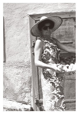 Ari wears a stylish dress with a straw hat and sunglasses while holding a large box of pears in the 1970s