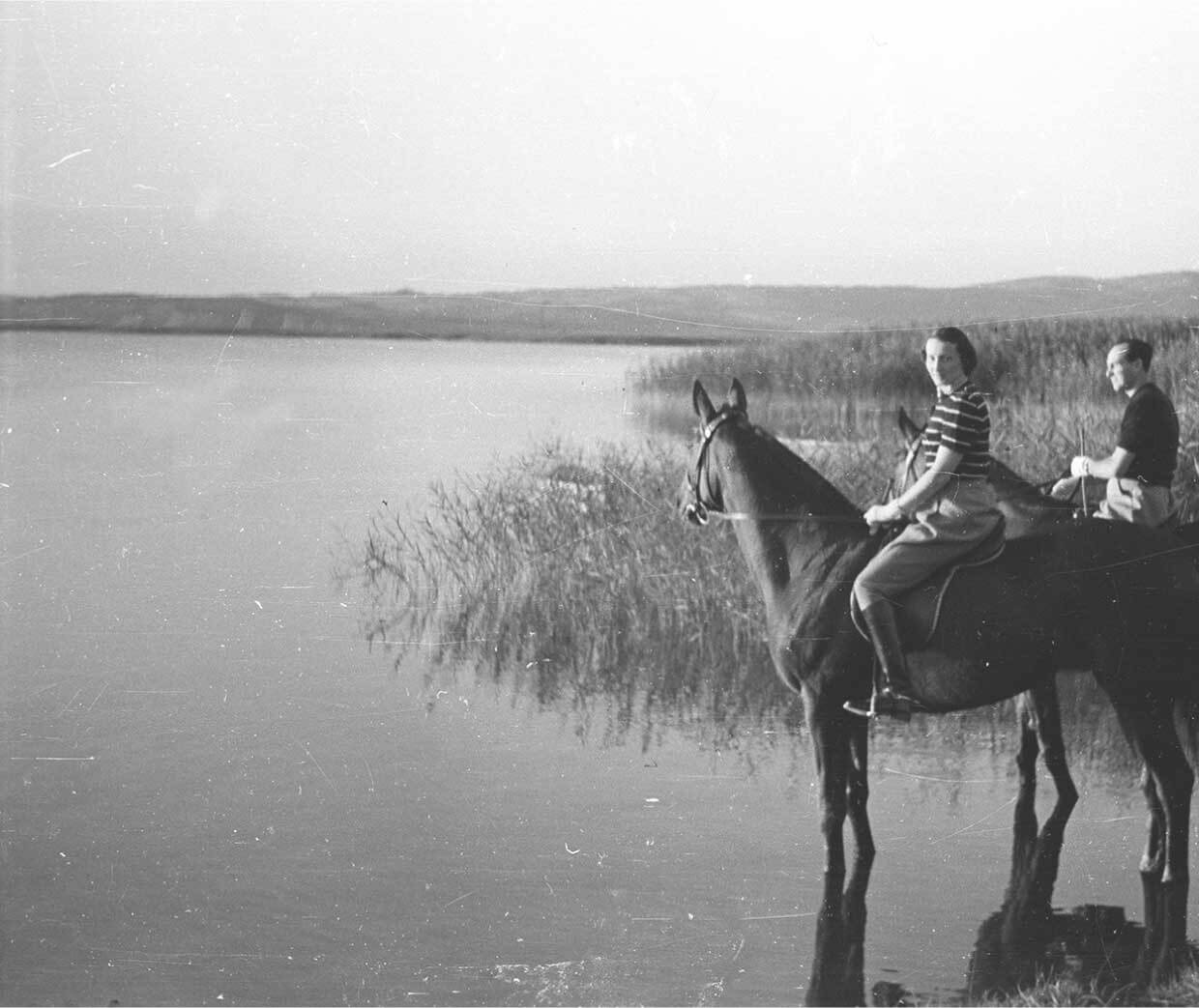Woman and man on horses by swampy lake