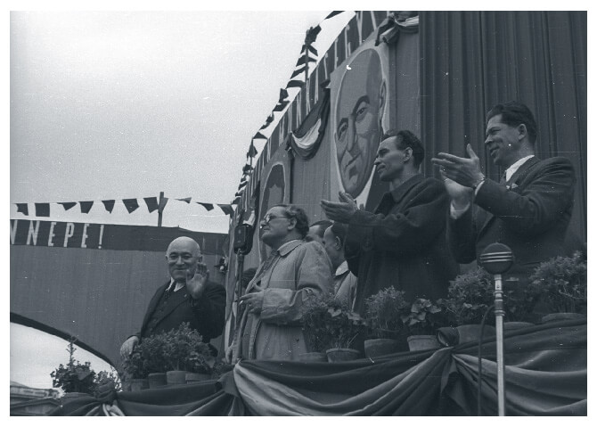 Mátyás Rákosi next to árpád Szakasits and László Rajk and György Marosán clapping on a podium in Heroes' Square
